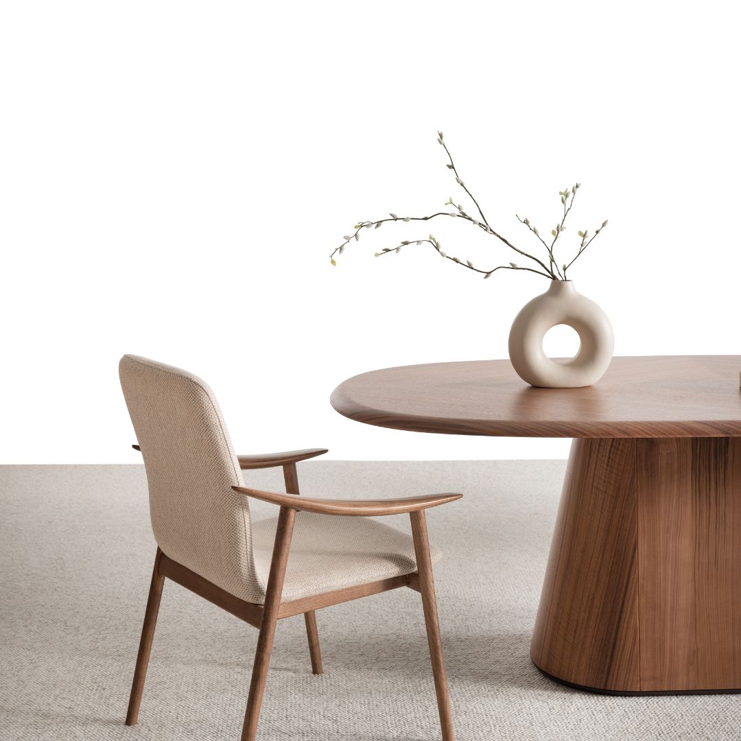 Близък план на ръба на масата и текстилния стол до нея, подчертаващ меките форми и топлия дървесен цвят.