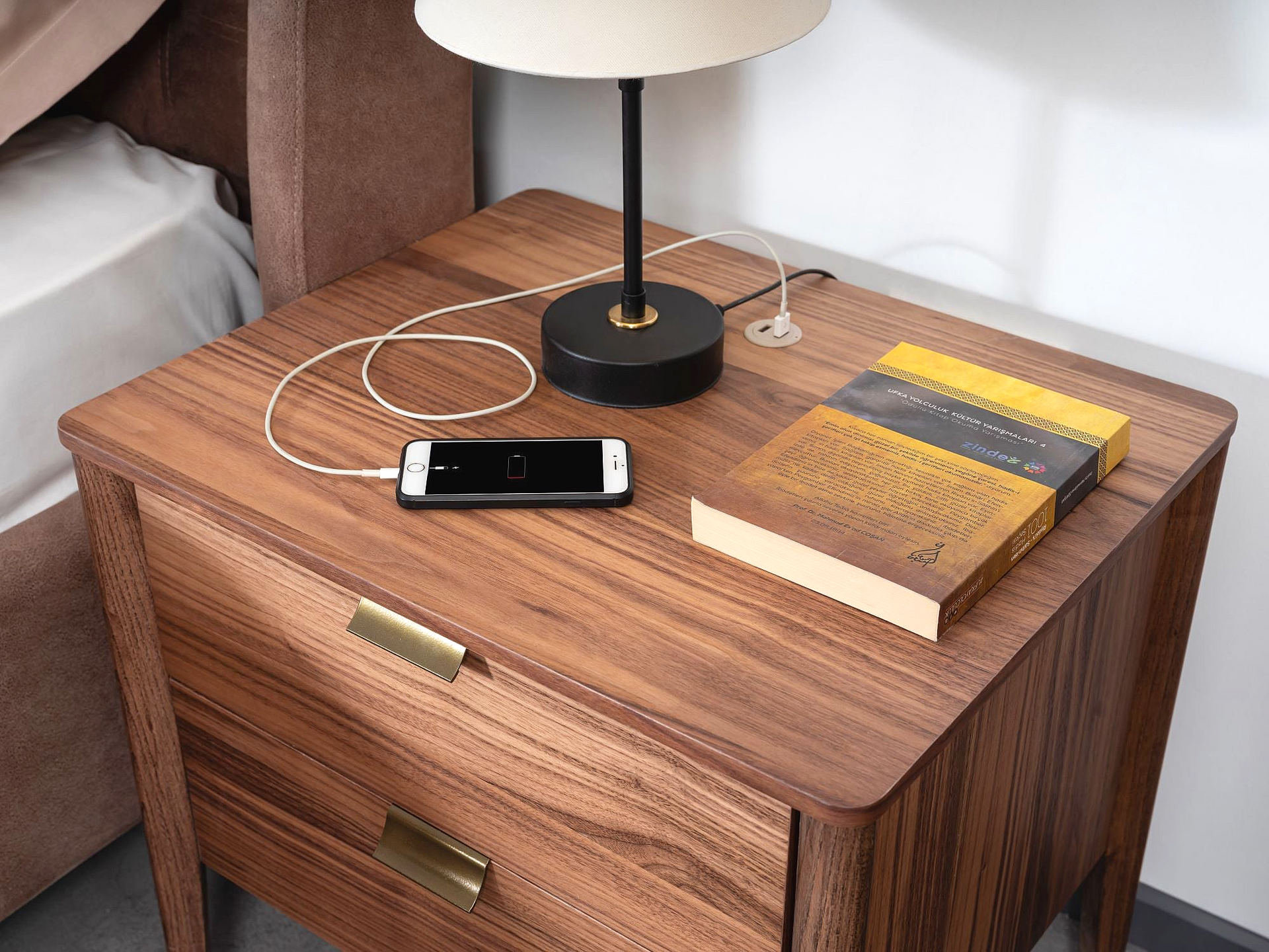 a nightstand with a phone, books and a lamp on it